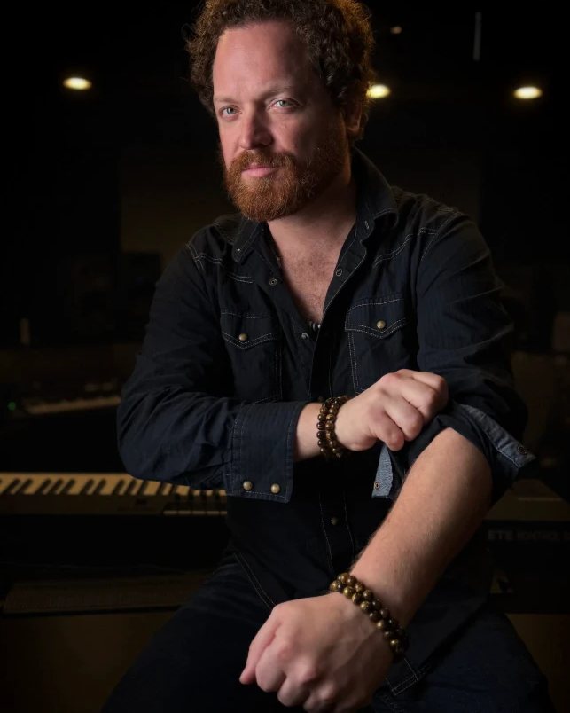 Dave Menzo seated in a recording studio, sleeves rolled