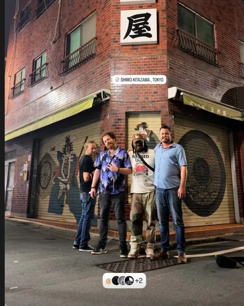 Dave Menzo and the band on a street corner in Shimokitazawa at night, under a 玉井屋 sign